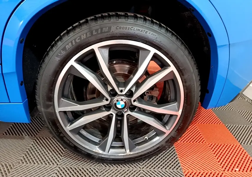Gros plan sur la roue avant droite d’un BMW X2 bleu, jante alliage à double branche en V.