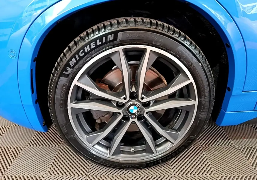 Gros plan sur la roue avant droite d'une BMW X2 bleu avec jante alliage et pneu Michelin visible.