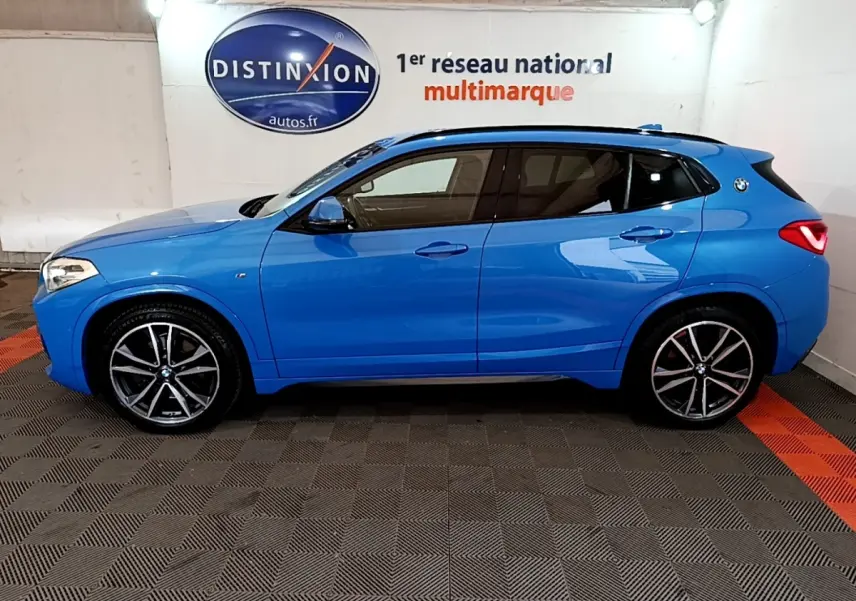 BMW X2 sDrive20i M Sport bleu en vue profil droit dans un showroom avec jantes alliage et toit noir.