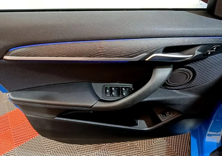 Vue intérieure de la porte avant gauche bleu de la BMW X2 sDrive20i M Sport avec éclairage d'ambiance bleu et commandes vitres.