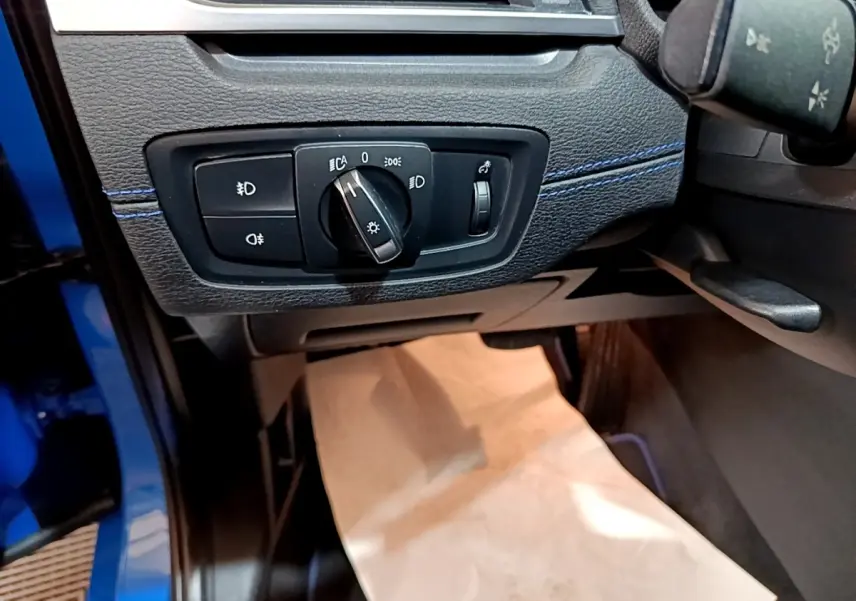 Détail du panneau de commande des phares côté gauche d’un BMW X2 bleu, avec surpiqûres bleues visibles.