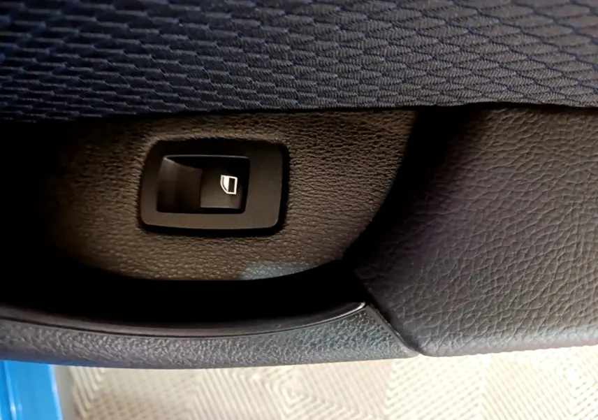 Gros plan sur le bouton de lève-vitre dans la portière intérieure noire d'une BMW X2 bleu sDrive20i M Sport.