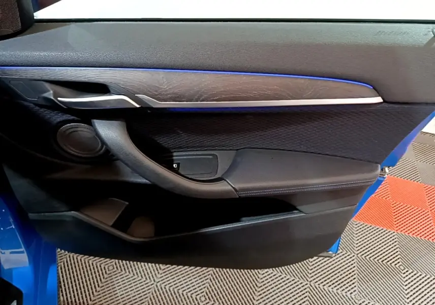 Vue intérieure côté gauche de la porte avant bleu de la BMW X2 avec garniture noire et bande décorative argentée.