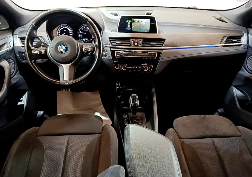 Vue intérieure avant de la BMW X2 sDrive20i M Sport 2019, tableau de bord noir avec écran tactile et volant cuir.
