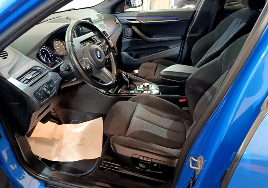 Vue intérieure côté conducteur d'une BMW X2 sDrive20i M Sport bleu avec sièges noirs et tableau de bord moderne.
