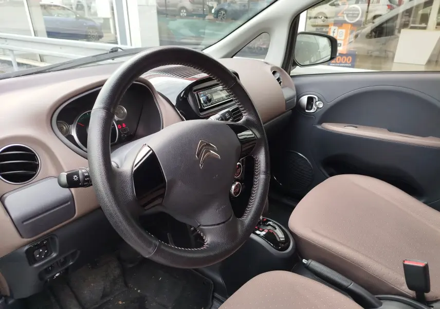 Vue intérieure côté conducteur du Citroën C-ZERO blanc Antarctique, montrant le volant, tableau de bord et sièges beige clair.