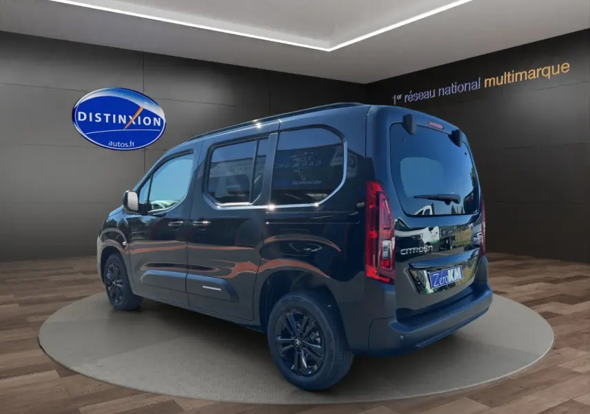 Citroën Berlingo noir vu en 3/4 arrière droit, avec vitres teintées et jantes noires dans un showroom.