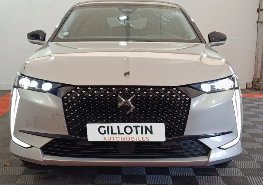Vue frontale d'une DS4 E-TENSE 225 gris clair avec calandre noire et phares LED allumés dans un garage.