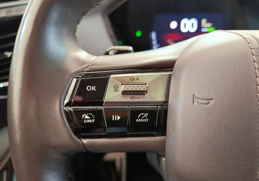 Gros plan sur les commandes gauche du volant cuir gris du DS4 E-TENSE 225 LA PREMIERE, affichage numérique en arrière-plan flou.