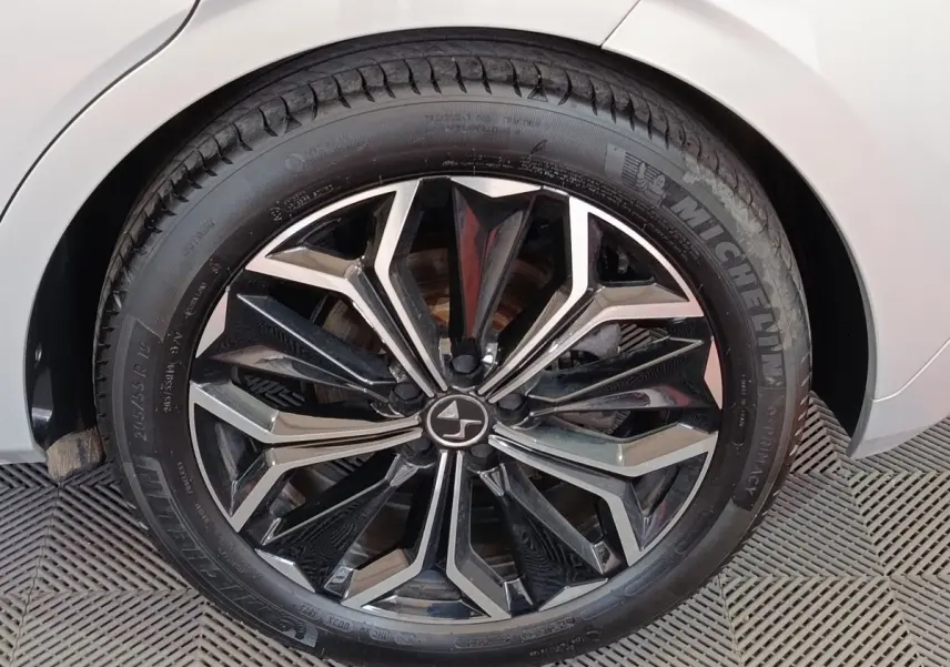 Gros plan sur la roue avant droite d'une DS4 E-TENSE gris clair avec jante noire et argentée au design géométrique.