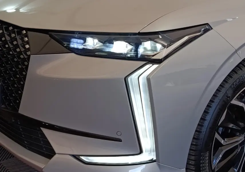Gros plan sur l'avant droit gris clair du DS4 E-TENSE 225 avec phares LED et feux diurnes en forme de flèche.