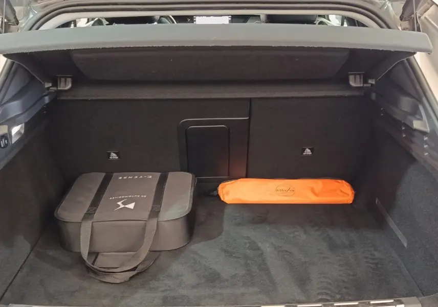 Coffre ouvert d'une DS4 E-TENSE 225 gris clair, montrant un sac noir et une trousse orange rangés à l'intérieur.
