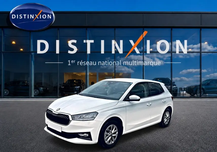 Vue 3/4 avant droite d'une Skoda Fabia blanche garée devant une vitrine avec logo Distinxion.