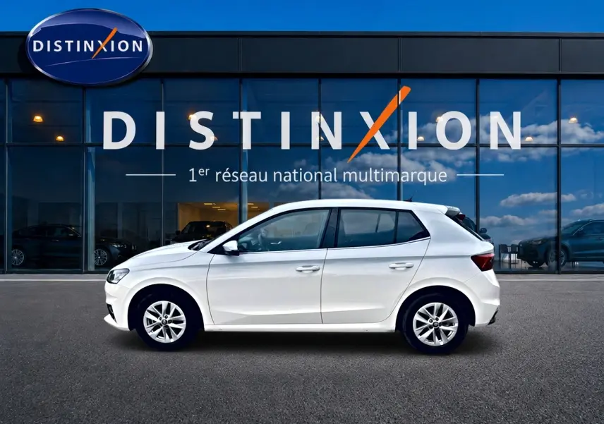 Vue latérale droite d'une Skoda Fabia blanche 2025 garée devant une vitrine avec logo Distinxion.