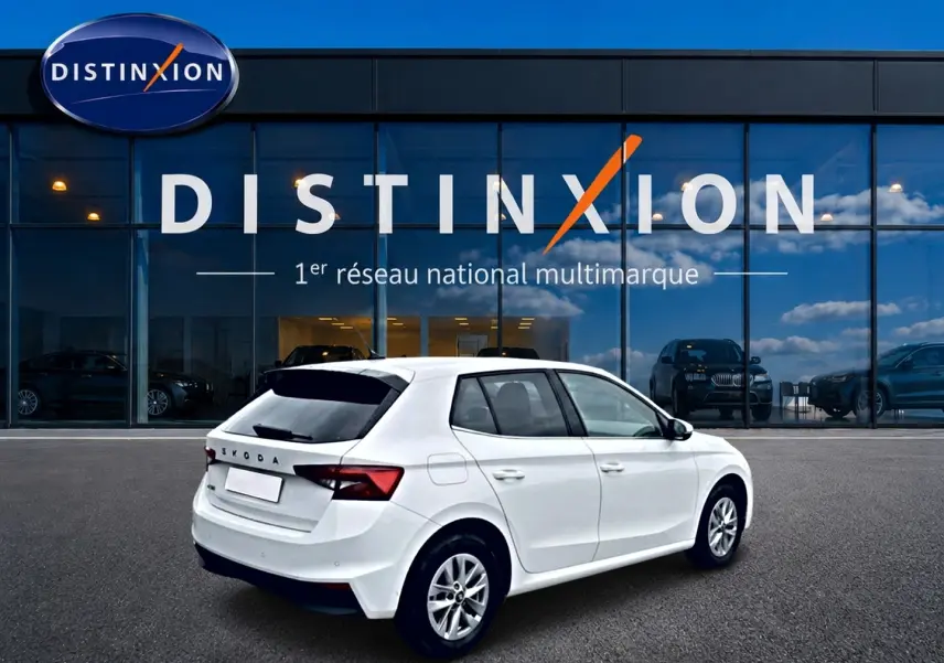 Vue 3/4 arrière droite d'une Skoda Fabia blanche 2025 avec jantes alu et vitres arrière teintées, devant un showroom Distinxion.