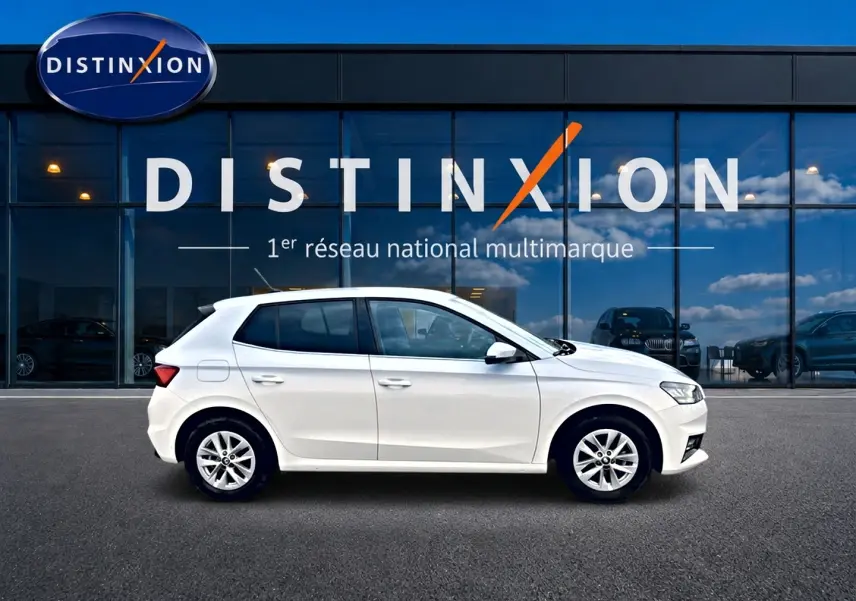 Profil droit d'une Skoda Fabia blanche 2025 garée devant une vitrine avec logo Distinxion.