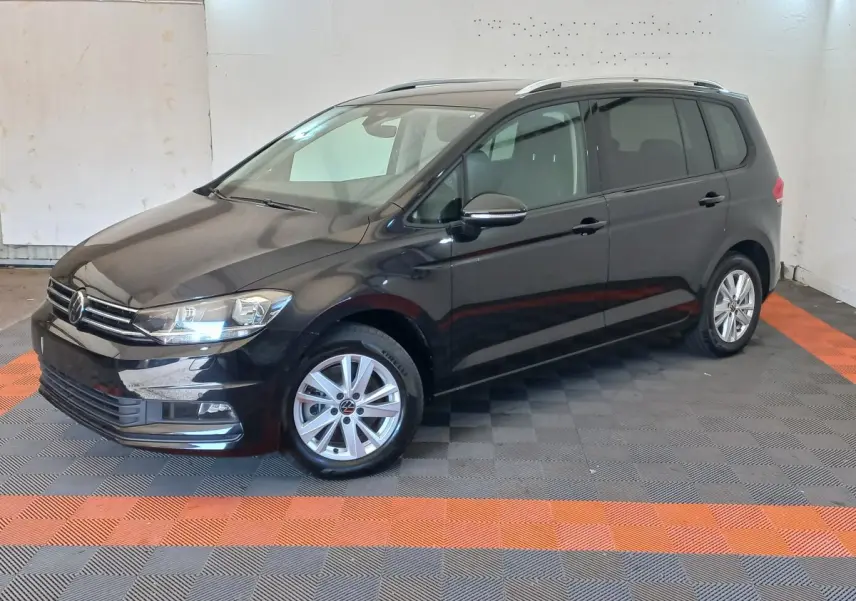 Volkswagen Touran noir vu en 3/4 avant droit, avec jantes alliage et barres de toit chromées visibles.