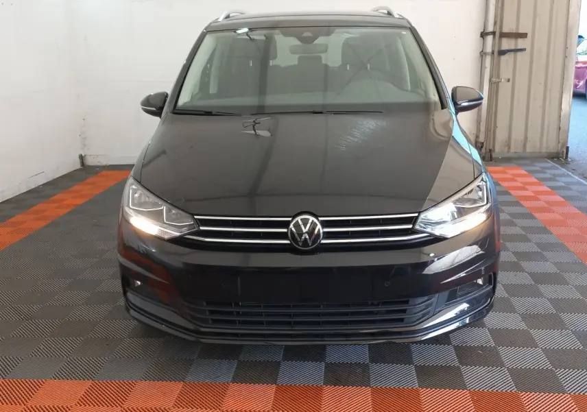 Vue frontale d'un Volkswagen Touran noir 2024 avec phares allumés dans un garage intérieur.