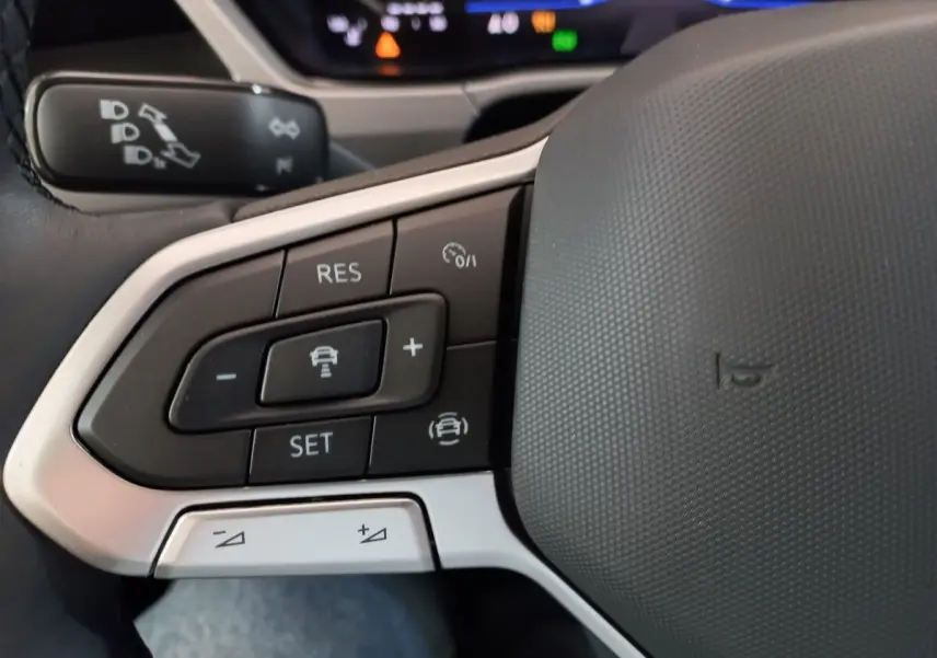 Gros plan sur les commandes de régulateur de vitesse au volant cuir gris du Volkswagen Touran noir 2024.