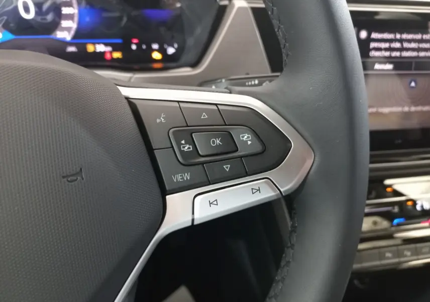 Gros plan sur le côté gauche du volant noir du Volkswagen Touran 2024 avec commandes multifonctions et affichage numérique en arrière-plan.