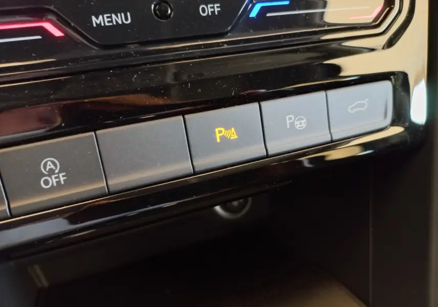 Gros plan sur les boutons de commande du tableau de bord noir du Volkswagen Touran 2024, avec témoin d'aide au stationnement allumé.
