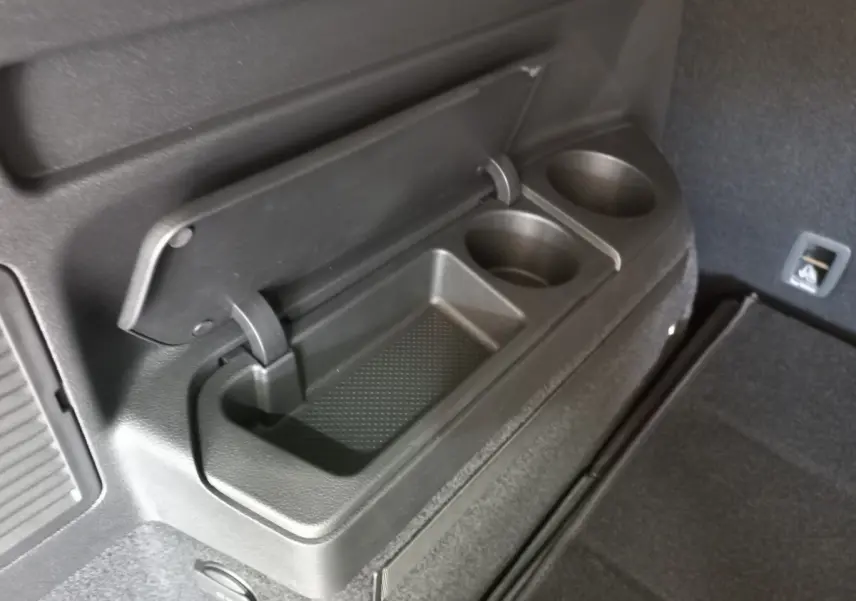 Détail du rangement avec porte-boissons intégré dans le coffre noir du Volkswagen Touran 2024, côté droit.