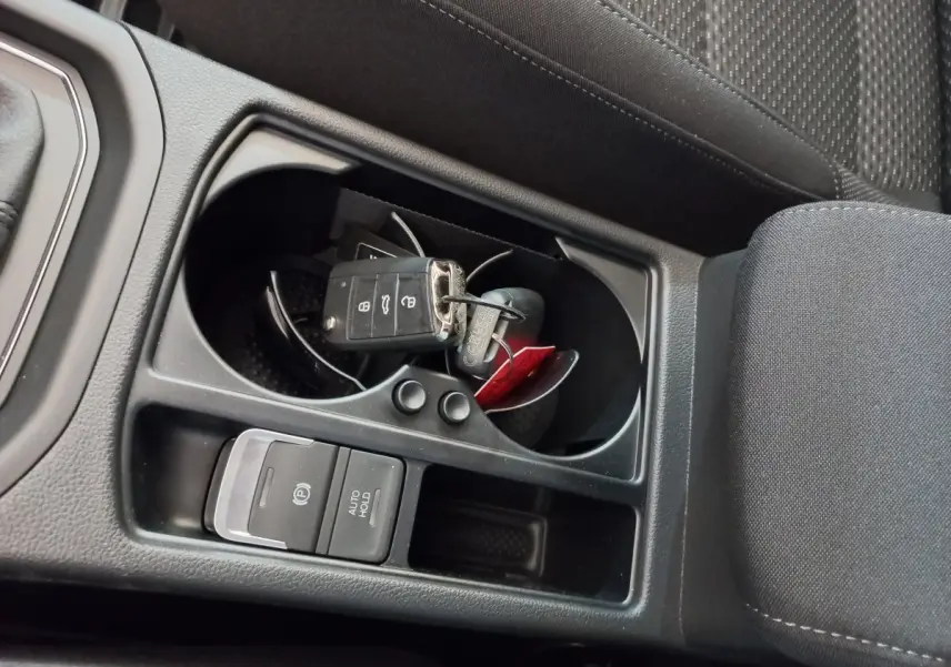 Gros plan sur la console centrale noire du Volkswagen Touran 2024 avec clés dans porte-gobelets et frein à main électrique.