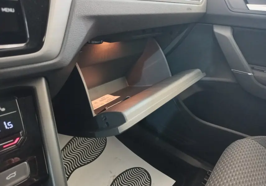 Intérieur du Volkswagen Touran 2024 noir, vue côté passager sur la boîte à gants ouverte avec éclairage intérieur.