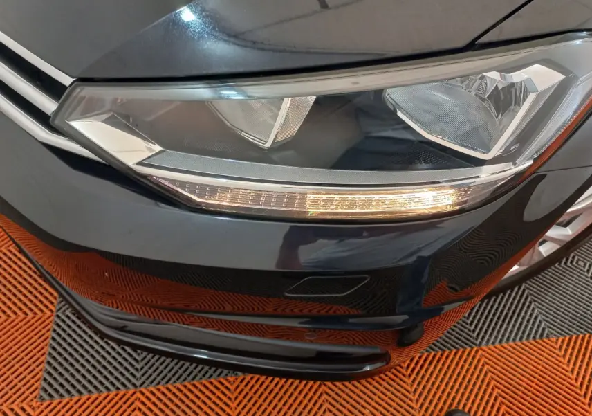 Gros plan sur le phare avant droit d’un Volkswagen Touran noir 2024 avec clignotant allumé.