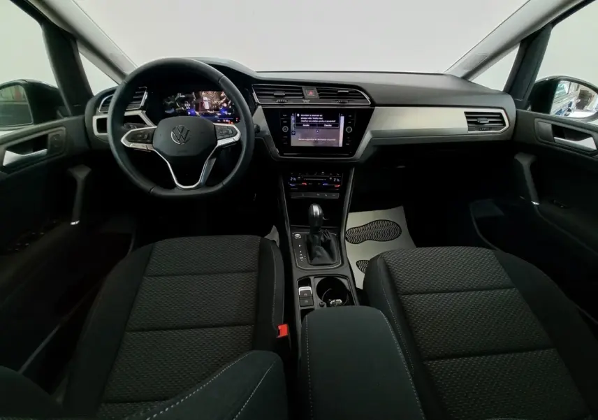 Vue intérieure avant du Volkswagen Touran 2024 noir, tableau de bord moderne avec écran tactile central et volant multifonctions.