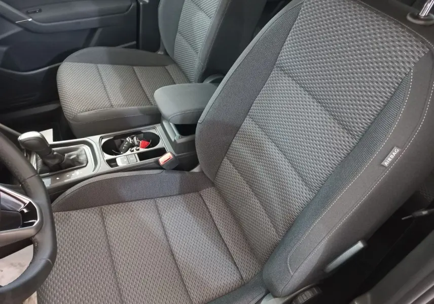 Vue intérieure rapprochée des sièges avant gris foncé du Volkswagen Touran 2024 avec console centrale et levier de boîte automatique.