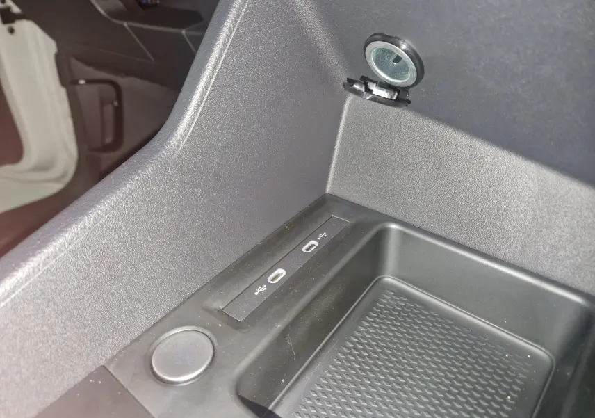 Gros plan sur la console centrale noire du Volkswagen Caddy Maxi blanc, montrant deux ports USB et une prise 12V.