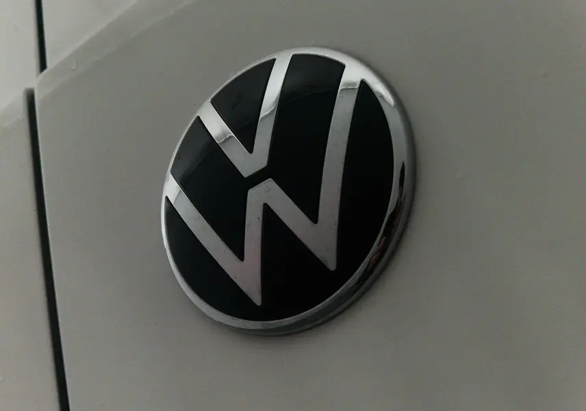 Gros plan sur l'emblème Volkswagen noir et chrome sur la carrosserie blanche du Caddy Maxi 2025.