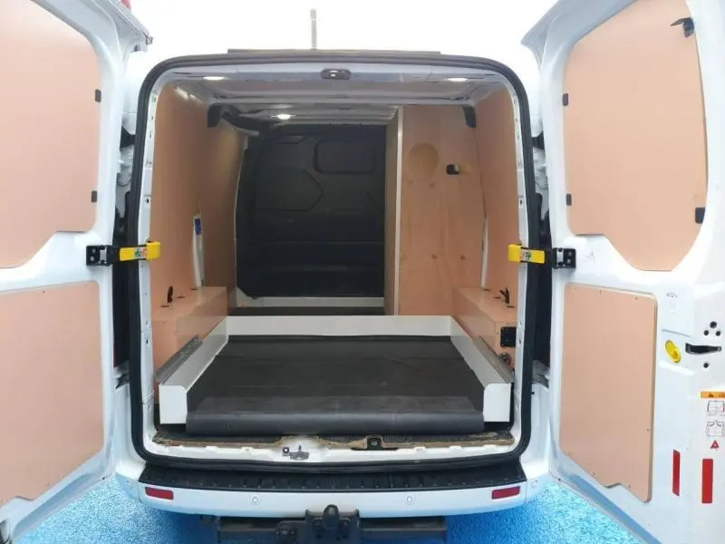 Vue arrière ouverte du Ford Transit Custom blanc glacier montrant l'intérieur aménagé avec panneaux bois et plancher noir.