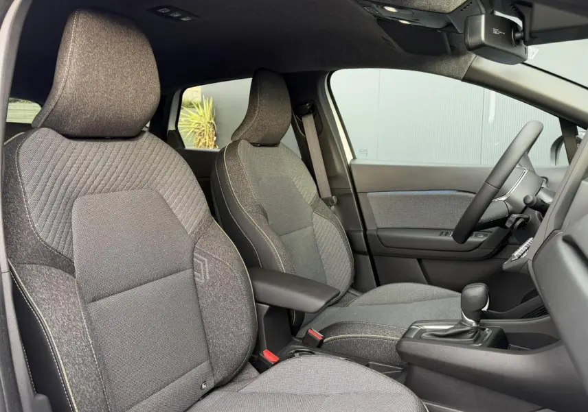 Vue intérieure côté droit du Renault Captur 2025, sièges tissu gris avec console centrale et volant visible.