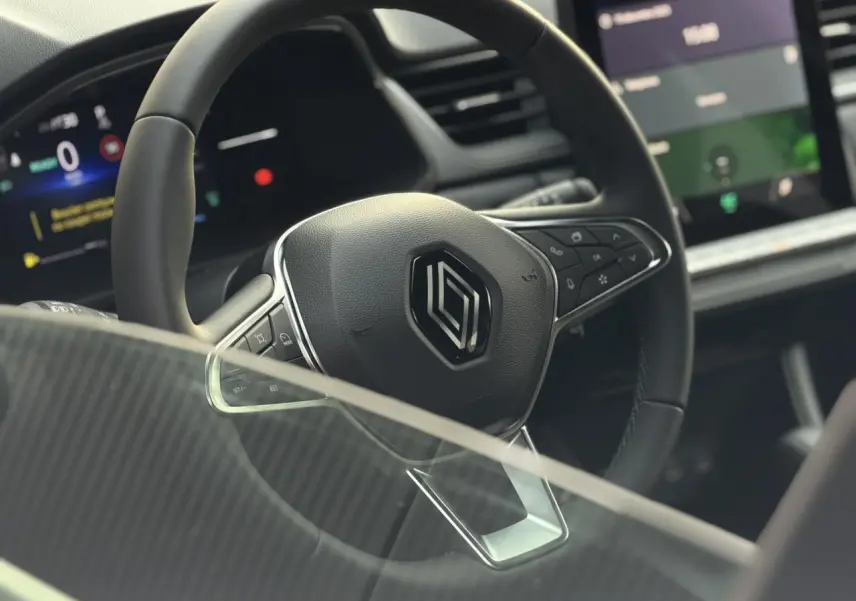 Gros plan sur le volant noir au logo Renault du Captur 2025, avec tableau de bord numérique et écran tactile visible en arrière-plan.