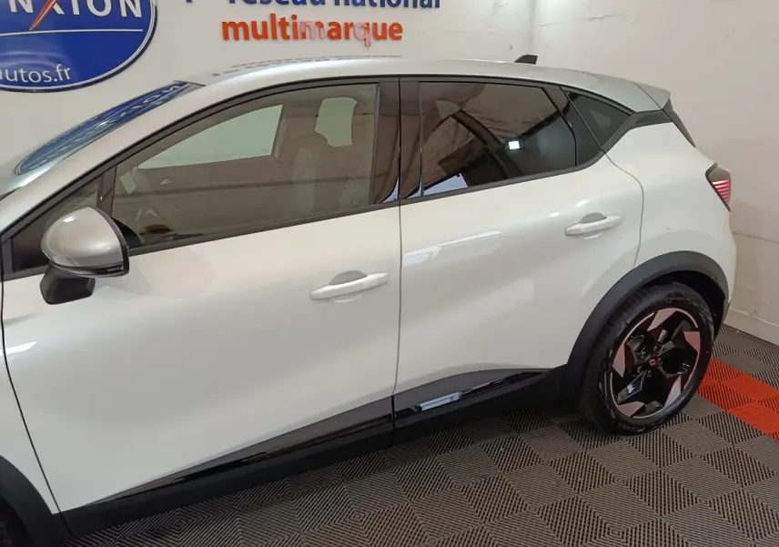Vue de profil côté gauche d'un Renault Captur blanc 2025 avec jantes noires et détails noirs sur les bas de caisse.