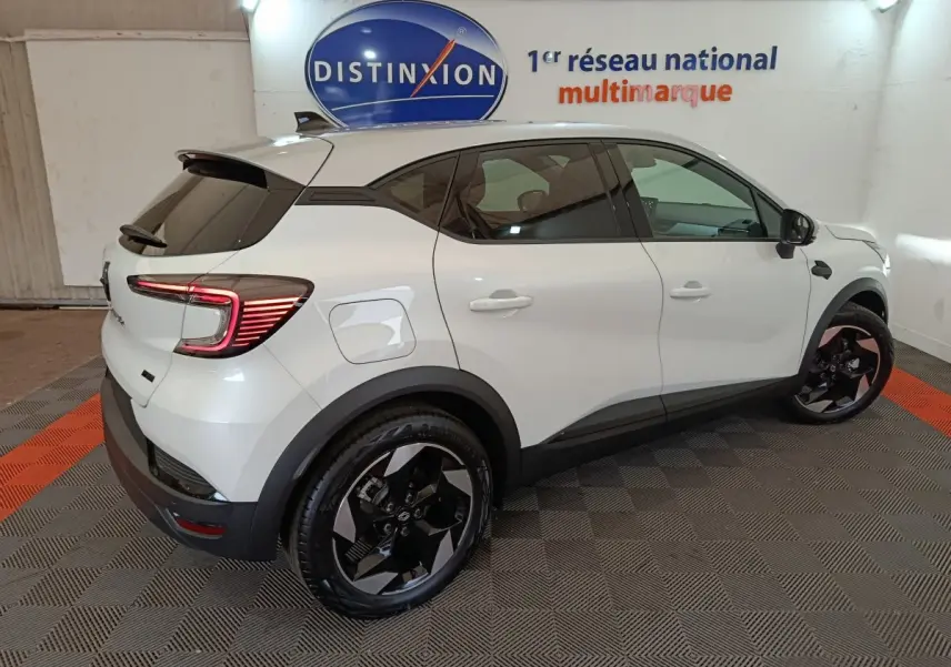 Vue 3/4 arrière droite du Renault Captur Techno E-Tech blanc, avec jantes noires et feux arrière LED allumés.