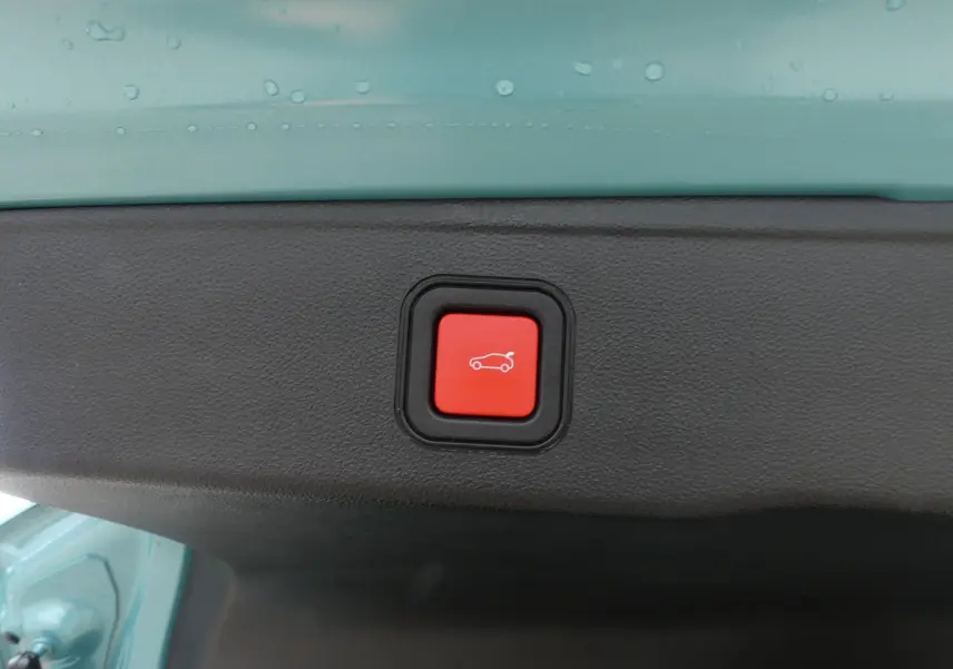 Bouton rouge d'ouverture électrique du hayon sur le coffre d'un Jeep Avenger bleu métallisé, vue intérieure du coffre.