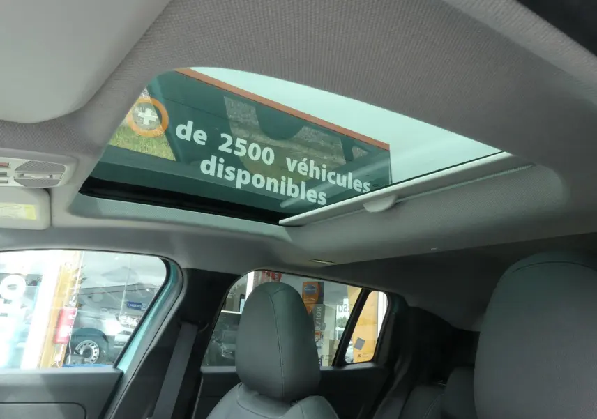 Vue intérieure du toit ouvrant en verre et des sièges avant noirs du Jeep Avenger bleu métallisé 2024.