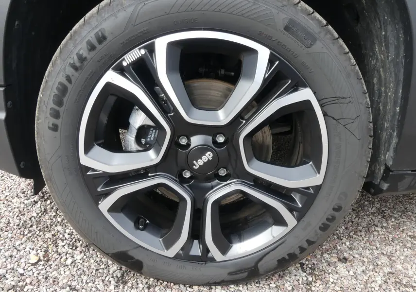 Gros plan sur la jante alliage 18 pouces noire et argentée avec logo Jeep, montée sur pneu Goodyear.