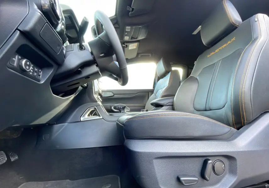 Intérieur côté conducteur du Ford Ranger Wildtrak 2025, sièges cuir noirs avec surpiqûres orange et logo Wildtrak brodé.