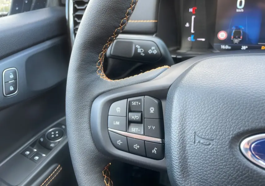 Gros plan sur le volant cuir noir avec surpiqûres orange du Ford Ranger Wildtrak 2025, boutons multifonctions visibles.