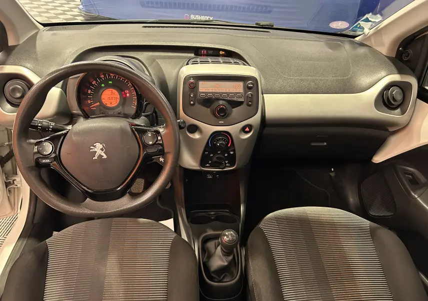 Vue intérieure avant de la Peugeot 108 blanche, montrant le volant, la console centrale avec radio et la boîte manuelle.