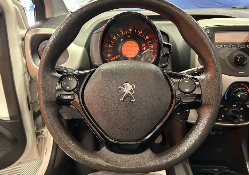 Vue rapprochée du volant noir de la Peugeot 108 blanche de 2014 avec tableau de bord et commandes visibles.