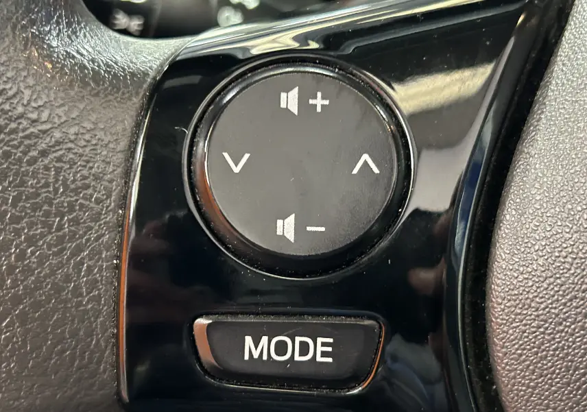 Gros plan sur les commandes audio au volant noir d'une Peugeot 108 blanche, boutons volume et mode visibles.