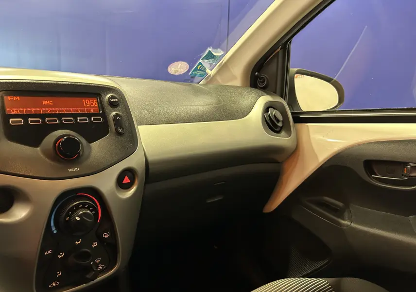 Vue intérieure côté passager du tableau de bord et de la portière d'une Peugeot 108 blanche de 2014 avec commandes de climatisation et radio visibles.