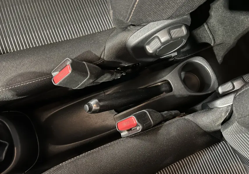 Gros plan intérieur sur la console centrale noire entre les sièges avant en tissu rayé gris et noir d'une Peugeot 108 blanche.