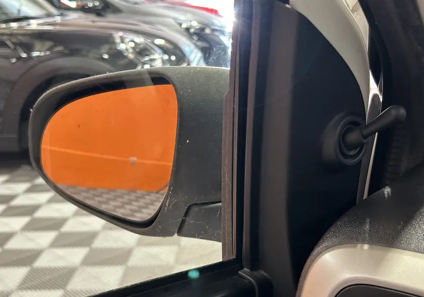 Vue rapprochée du rétroviseur extérieur gauche d'une Peugeot 108 blanche, avec reflet d'un mur orange en arrière-plan.