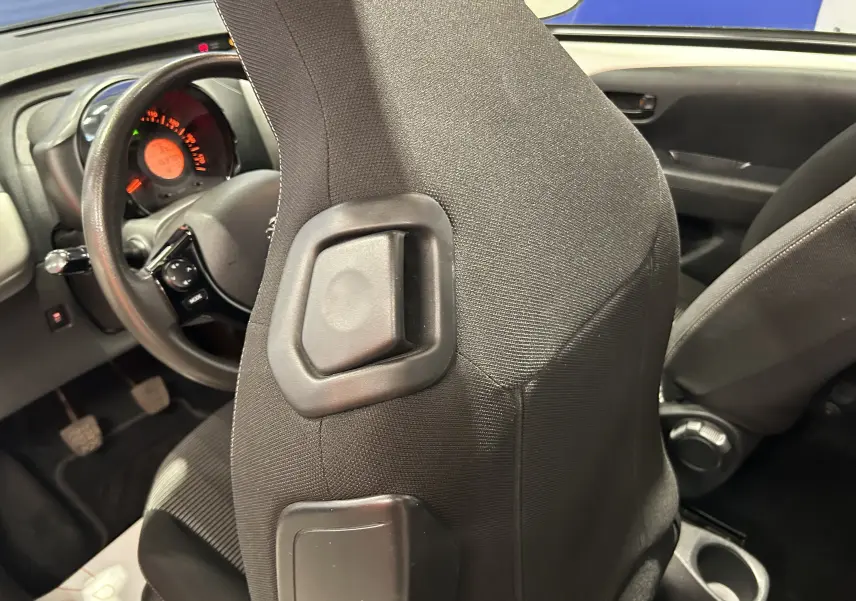 Vue intérieure rapprochée du siège conducteur en tissu noir et du tableau de bord d'une Peugeot 108 blanche de 2014.